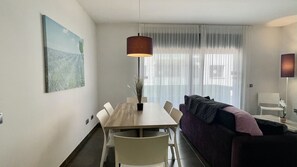 Uma sala de estar moderna com uma mesa de jantar, cadeiras, um sofá, uma luminária pendente e uma janela grande com cortinas leves.