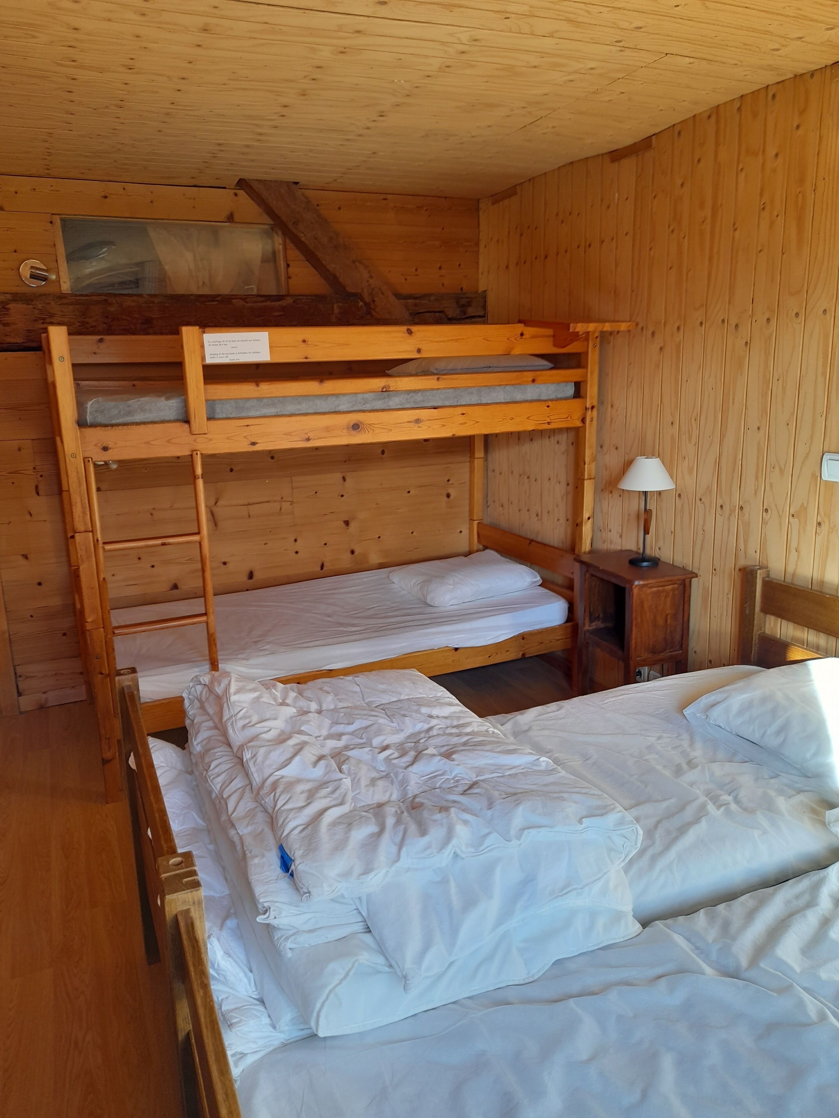 Dormitorio con literas, paredes de madera y una mesita de noche pequeña con lámpara.