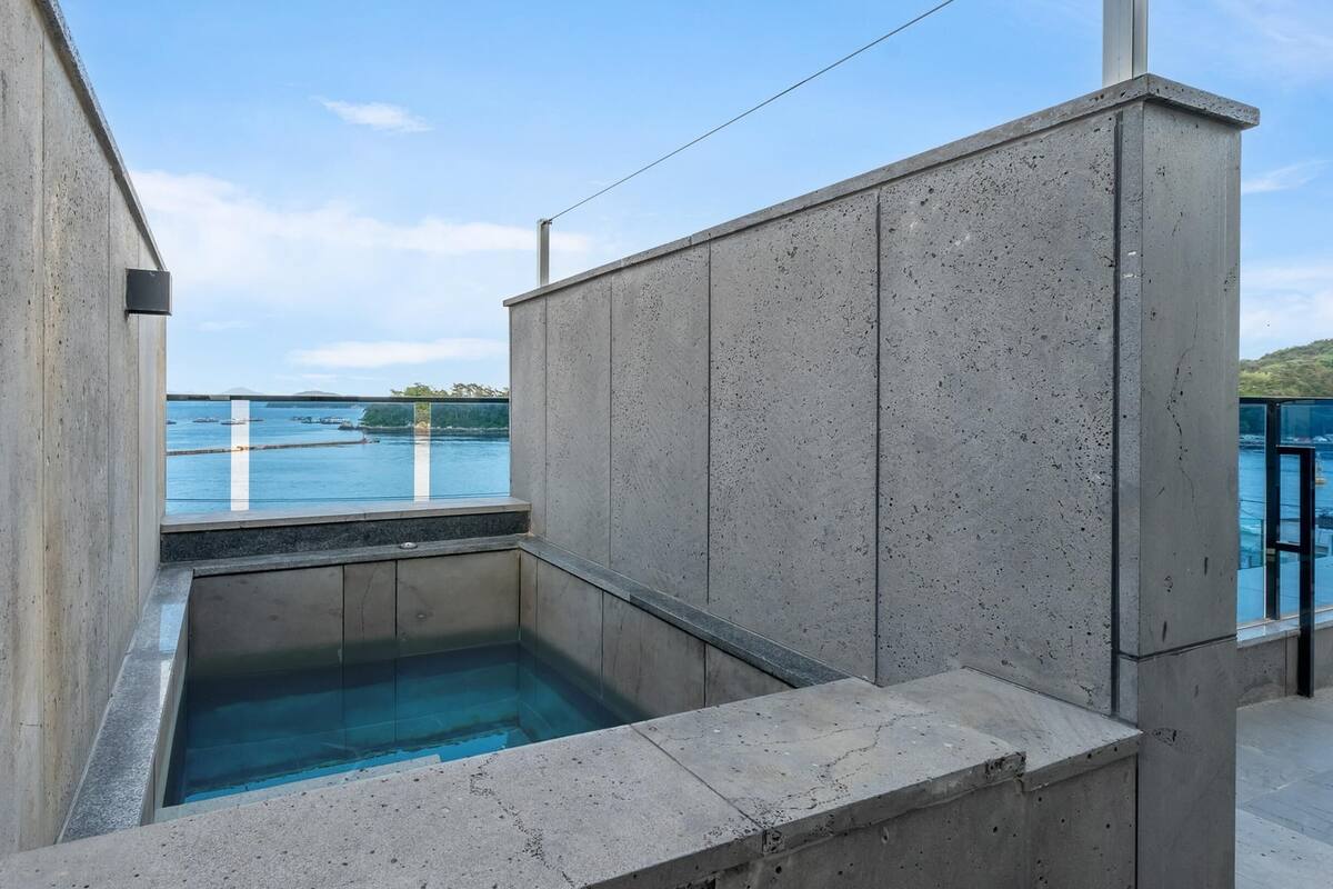 A modern outdoor pool area with a clear view of the sea and boats in the background.
