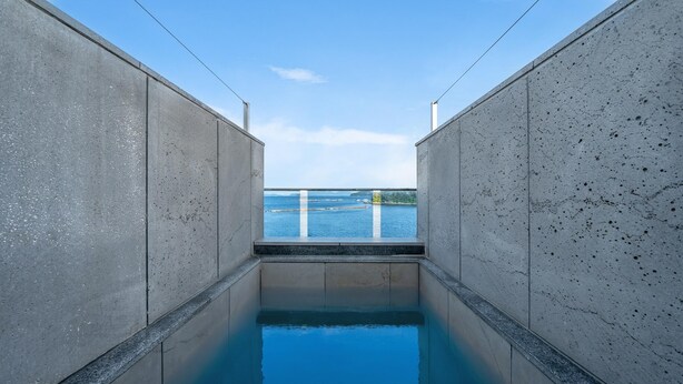Une petite piscine étroite d’où l’on a une vue dégagée sur la mer et le rivage, qui se trouve au loin.