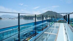 A glass-enclosed balcony with a view of a body of water and a distant island. - Changwon Healingtime Poolvilla Pension (Changwon)