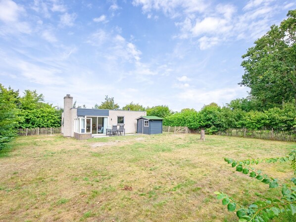 Une maison moderne avec un grand jardin, un potager clôturé et un ciel dégagé.