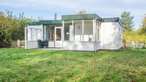 Une maison moderne de plain-pied, dotée d’une grande porte et de grandes fenêtres en verre, d’un patio couvert et d’une cour clôturée.
