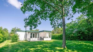 Une maison de plain-pied dotée d’un patio couvert, entourée d’une pelouse bien entretenue et d’arbres.