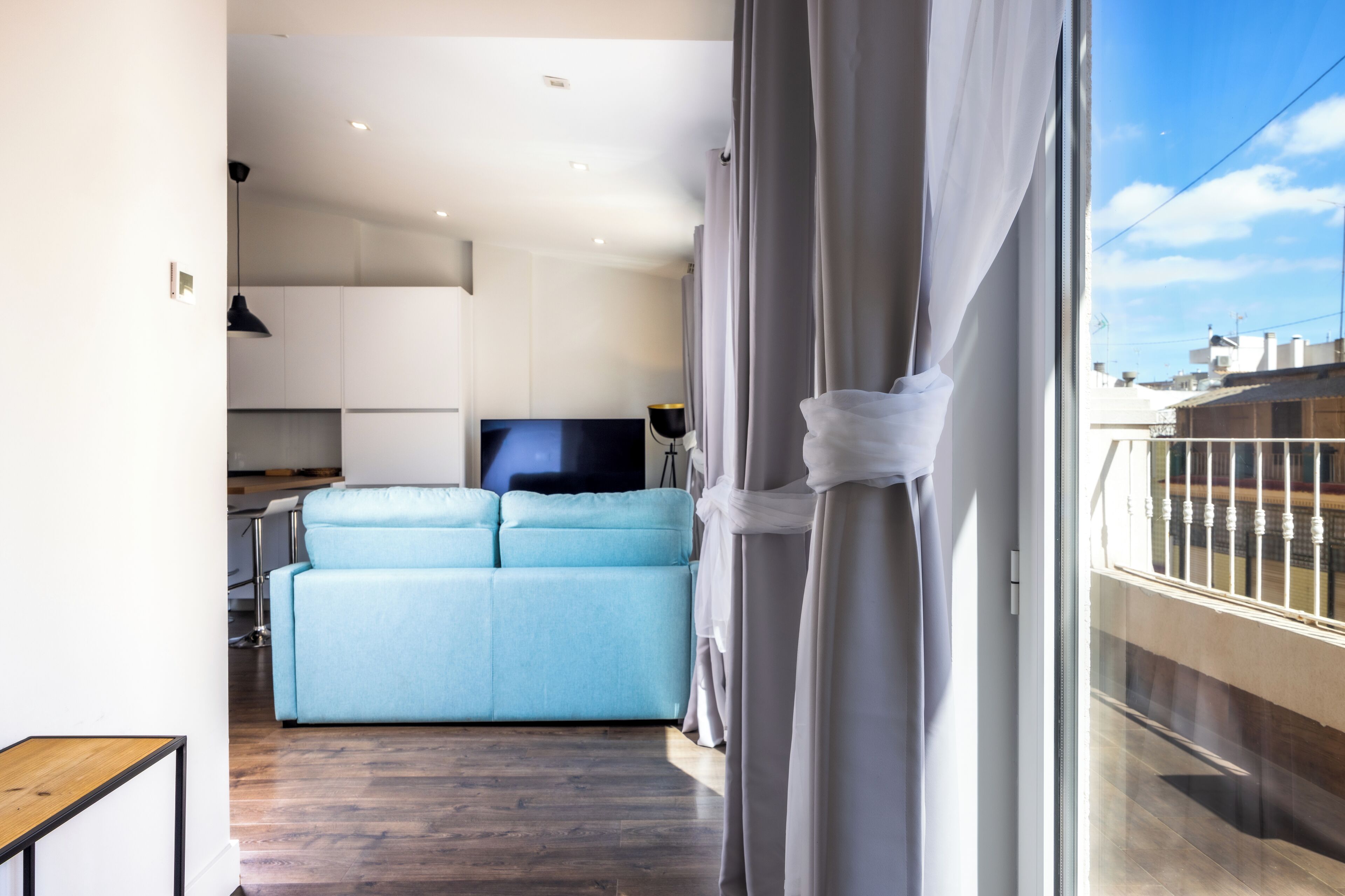 A modern living room with a light blue sofa, a flat-screen TV, and a balcony with a railing.