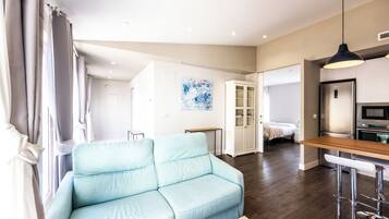 A modern living room with a light blue sofa, a wooden dining table, and a kitchen area with a refrigerator and oven.