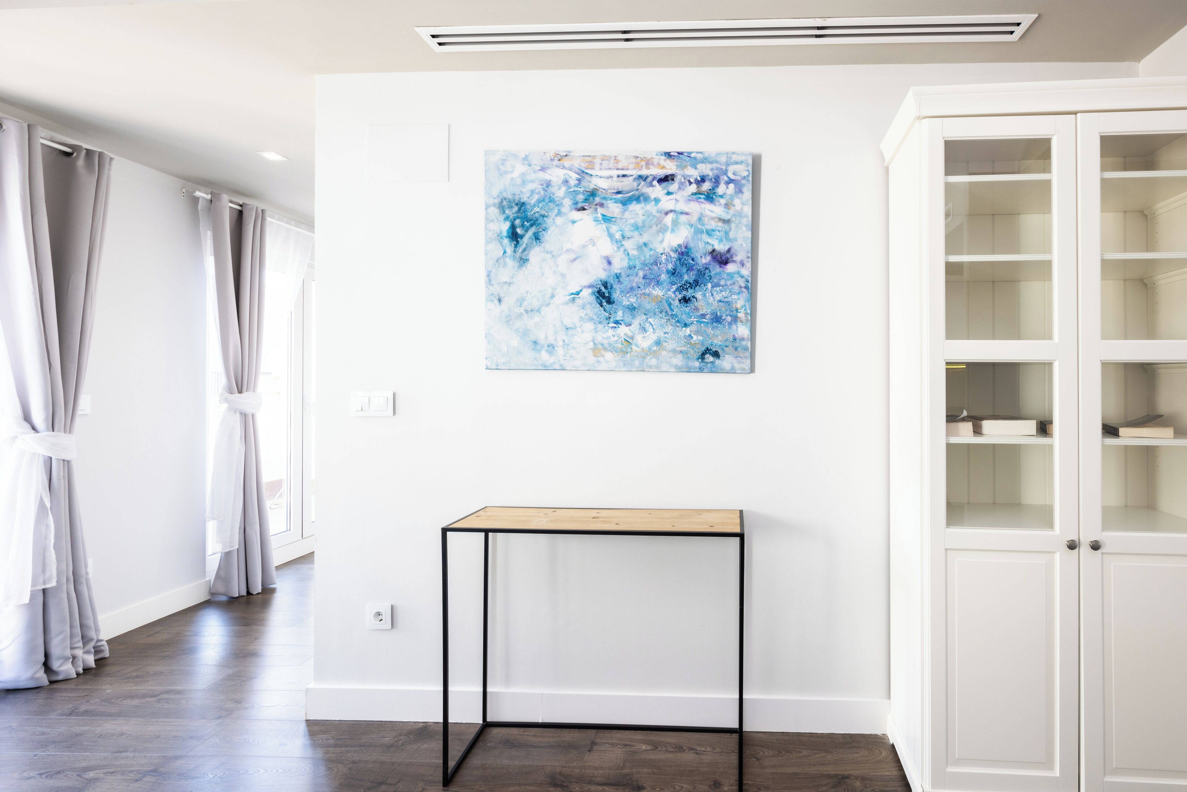 Una habitación con pared blanca, una mesa de madera y un armario blanco con puertas de cristal.