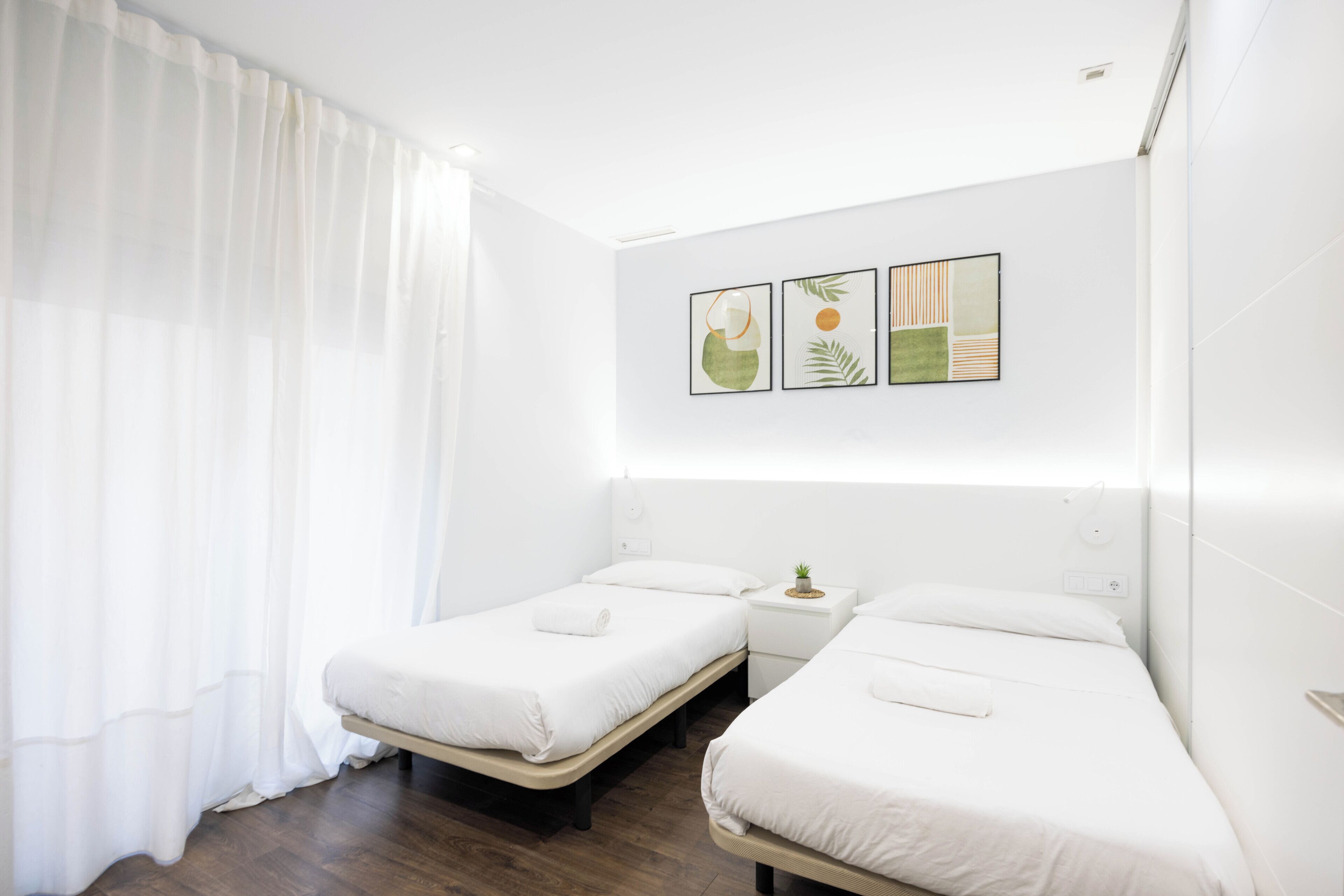 Una habitación de hotel con dos camas individuales, una mesita de noche con una planta y una pared decorada con tres cuadros enmarcados.