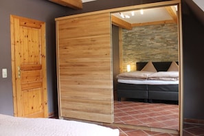 A bedroom with a wooden wardrobe, a bed with pillows, and a stone wall. - Holiday Maisonette Apartment "keilberg" (Annaberg-Buchholz)
