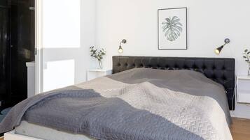 Un dormitorio moderno con una cama, cabecera, mesitas de noche y una planta enmarcada en la pared.