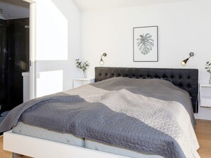 A modern bedroom with a bed, a headboard, bedside tables, and a framed plant on the wall.