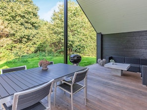 Une terrasse extérieure avec une table et des chaises, un barbecue et un coin salon agrémenté de coussins.
