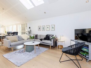 A modern living room with a grey sofa, a round coffee table, a black chair, a TV, and a bookshelf with board games.