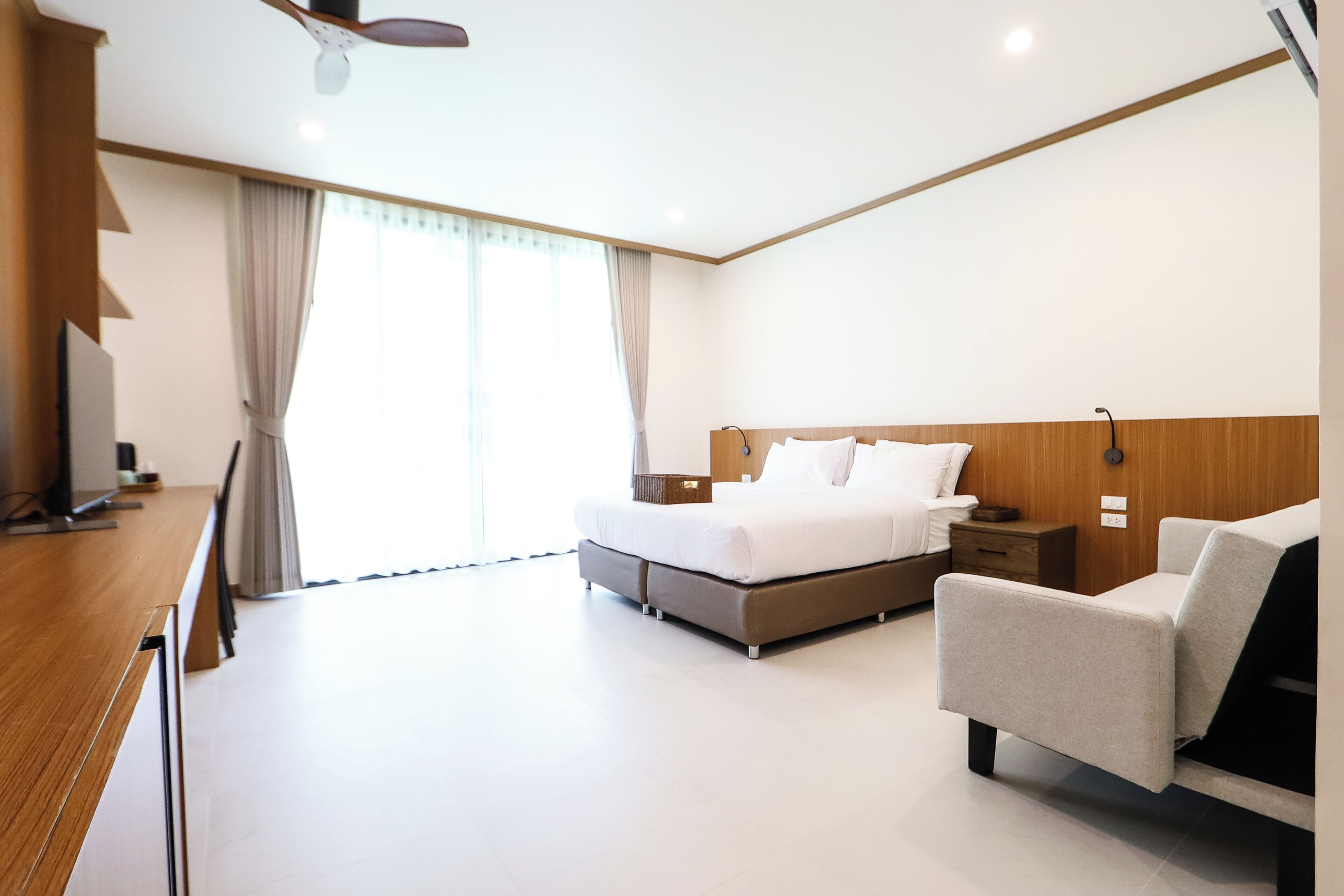 A modern hotel room with a bed, bedside table, chair, and a desk with a chair.