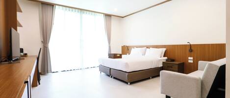 A modern hotel room with a bed, bedside table, chair, and a desk with a chair.