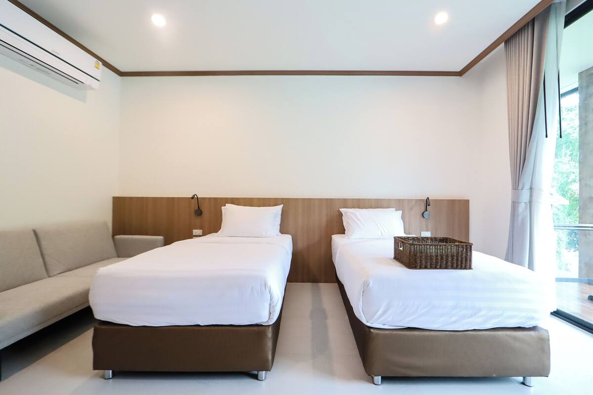 Une chambre d’hôtel avec deux lits, un canapé et une grande fenêtre avec des rideaux.