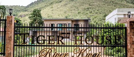 Una entrada con puerta y señalización que dice "Tiger House River Kway", un edificio moderno y un paisaje montañoso de fondo.