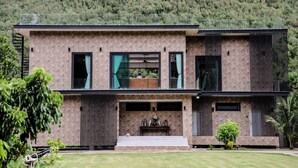 A modern two-story house with a stone facade, large windows, and a balcony. - Tiger House River Kwai (Si Sawat)