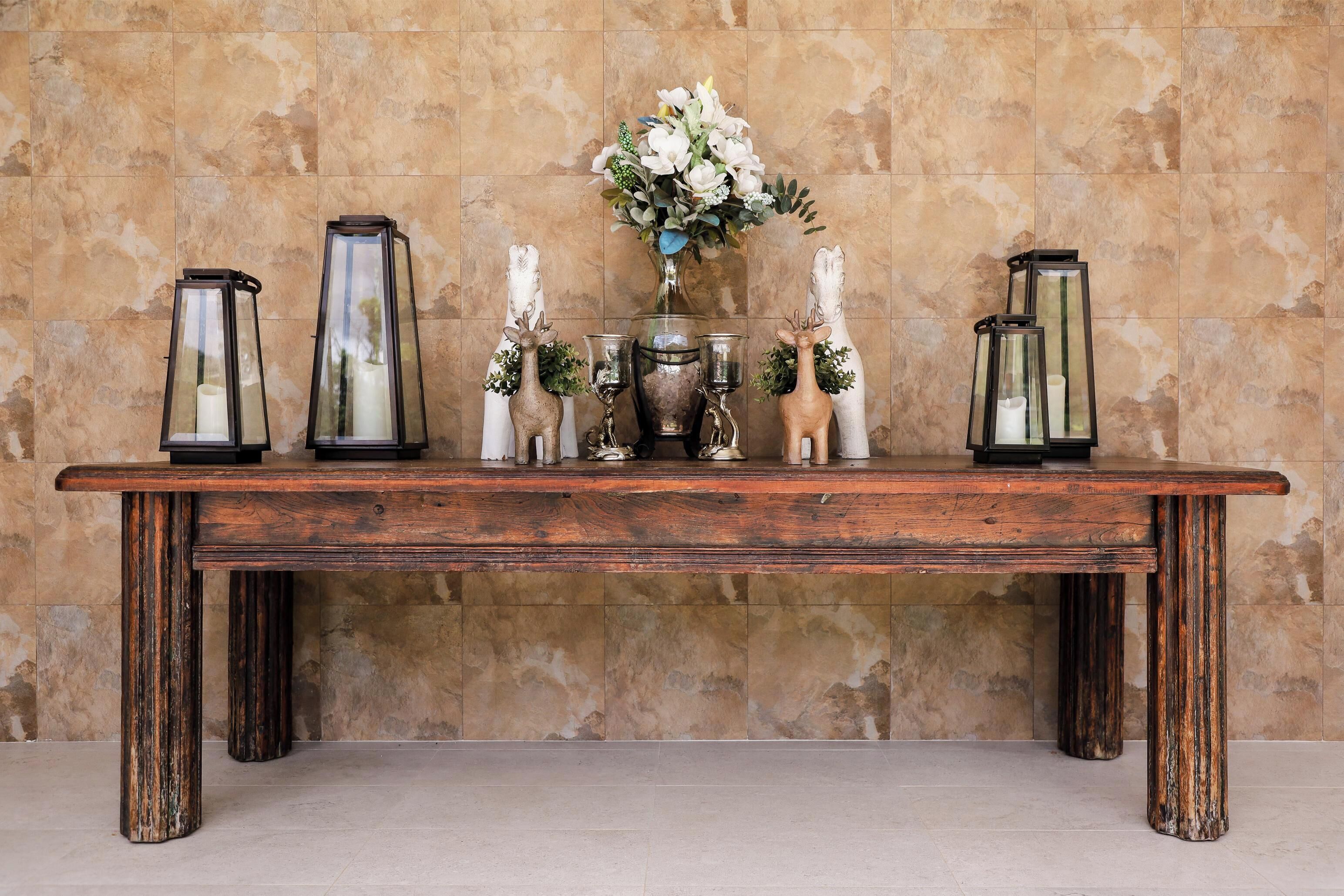 Une table en bois, ornée de lanternes en verre, de bougies et de figurines de cerfs décoratives, le tout placé devant un mur carrelé.