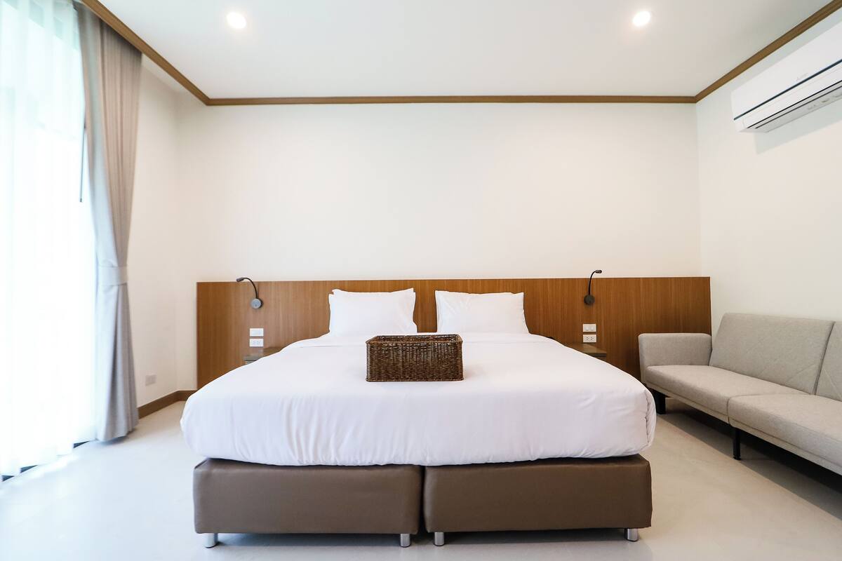 Une chambre d’hôtel moderne avec un grand lit, un canapé et une tête de lit en bois.