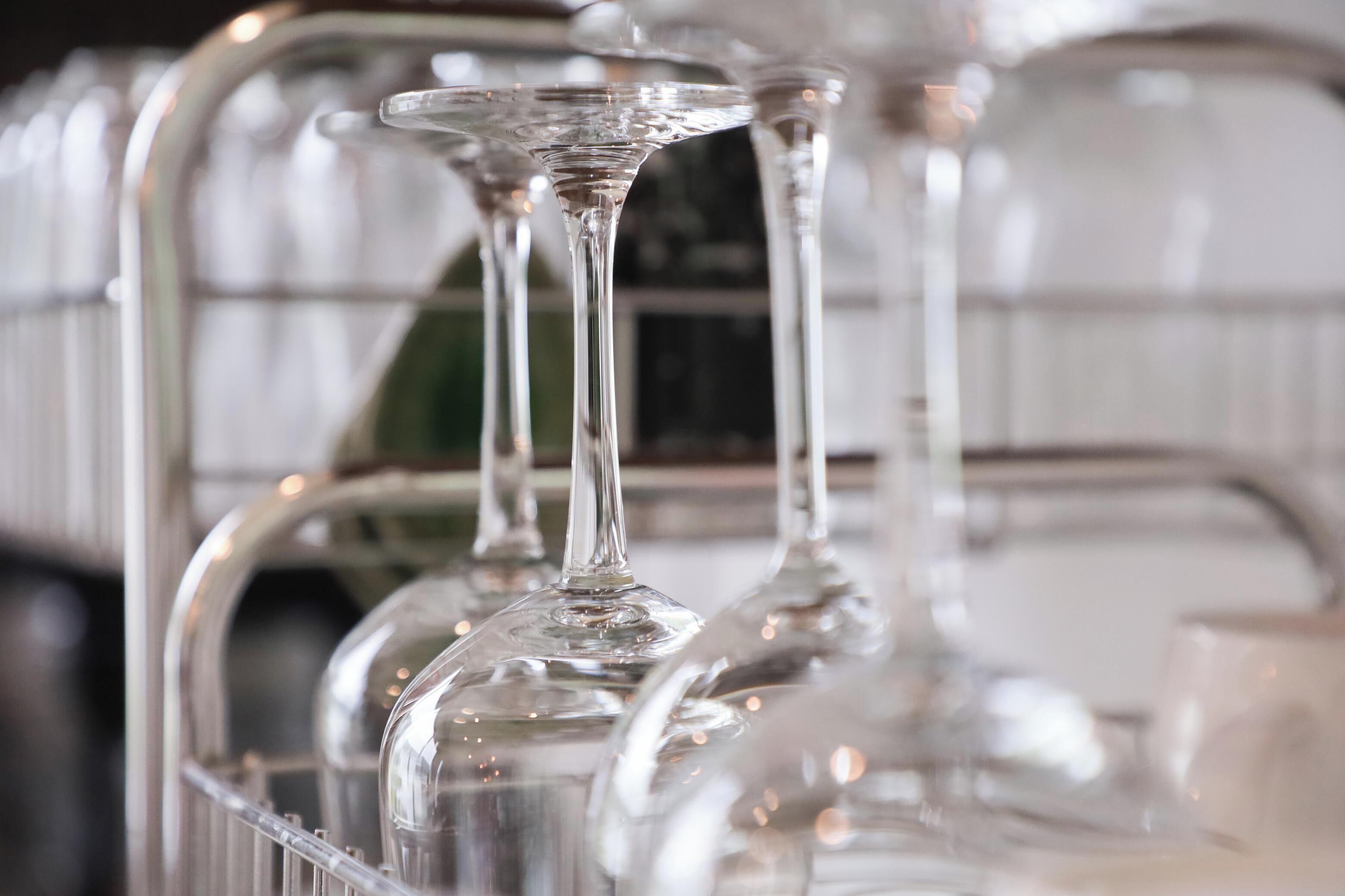 A row of clear, empty wine glasses on a rack.