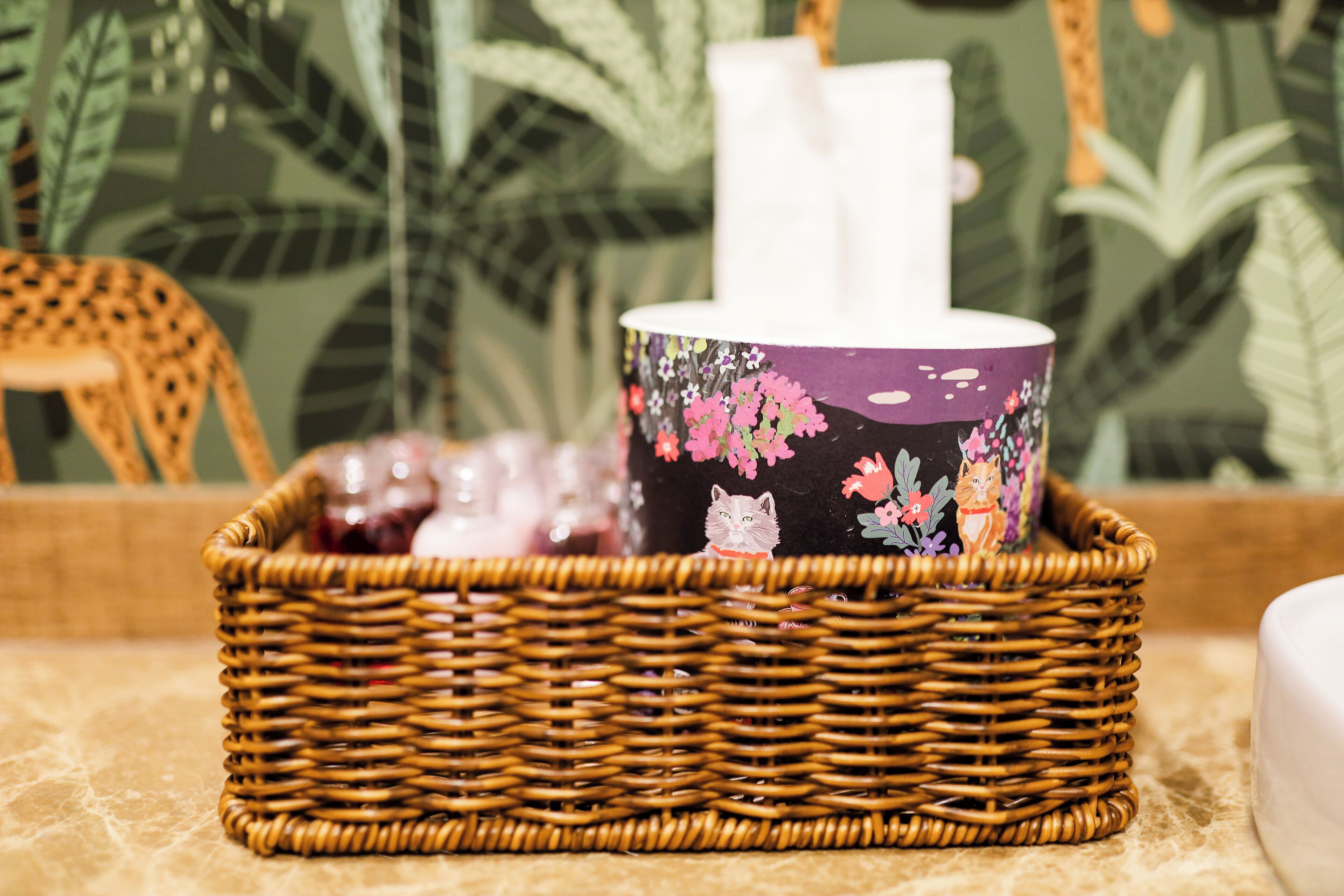 A wicker basket with a floral mug and a tissue box on a textured surface.
