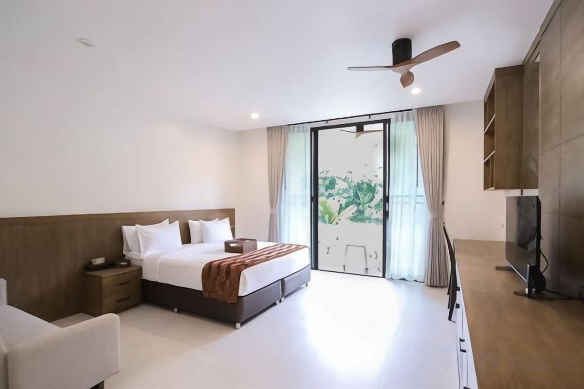Camera d'hotel moderna con un letto grande, una scrivania, una sedia, una TV e una porta scorrevole in vetro che dà su un balcone.