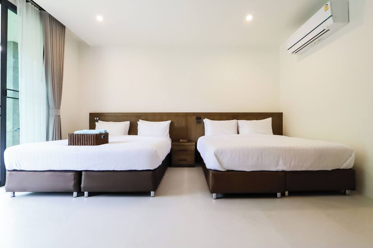 Une chambre d’hôtel avec deux lits, une tête de lit en bois, une petite table de chevet et un appareil de climatisation.