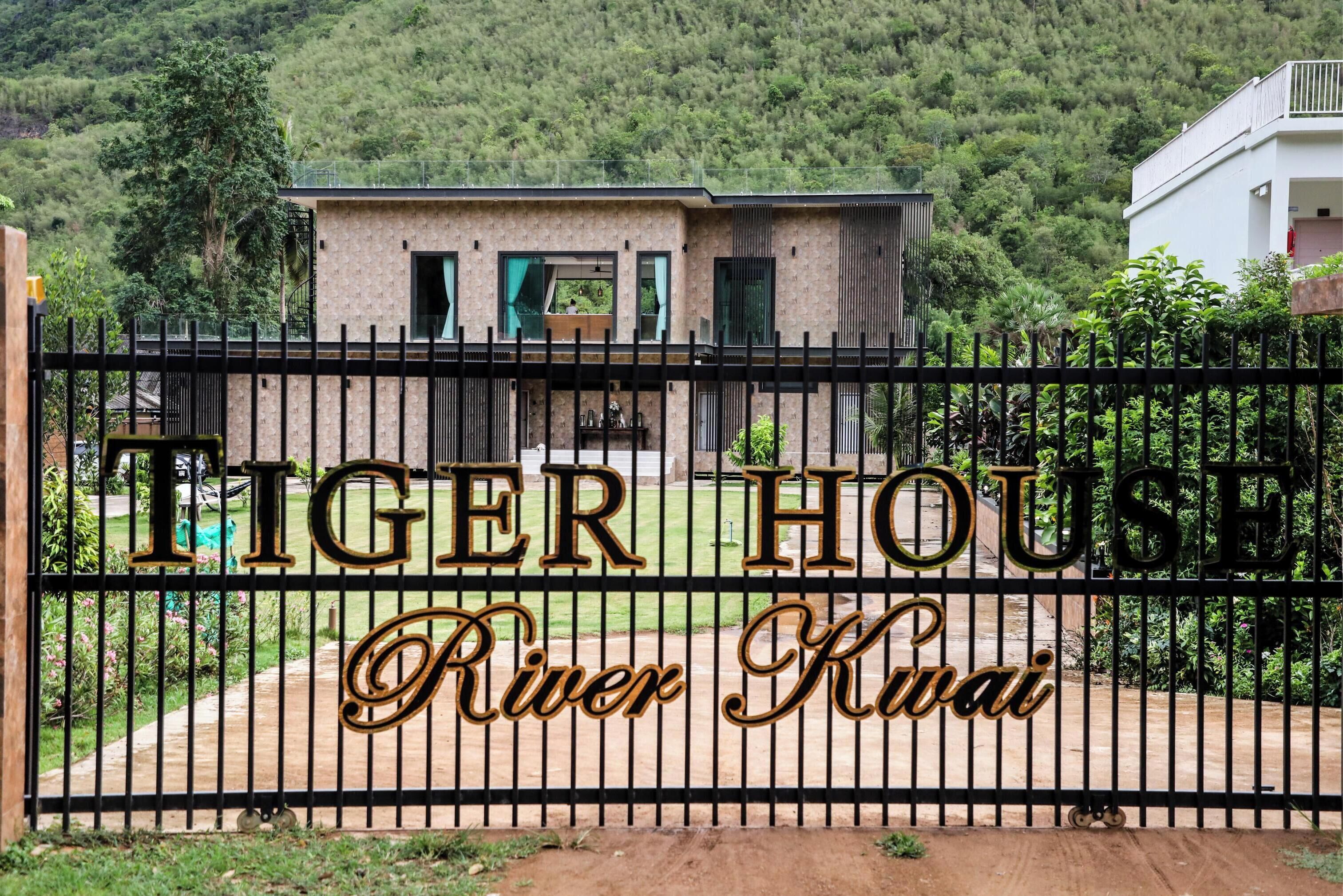 A gated entrance to a property named "Tiger House" with a view of a building and lush greenery in the background.