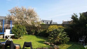 Un jardin avec une pelouse, une table en bois, deux chaises, un arbre et une clôture.