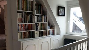 Une pièce avec un plafond en pente, un escalier blanc et une bibliothèque remplie de livres.