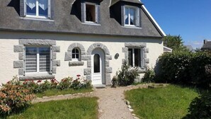Une maison à deux étages avec une façade en pierre, une entrée centrale et un chemin de gravier menant à la porte.