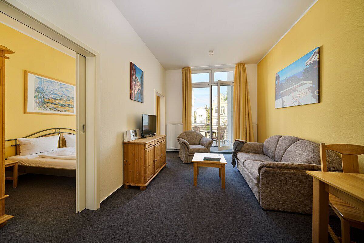 A hotel room with a bed, a wooden cabinet, a television, a sofa, a chair, and a table.