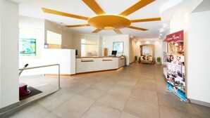 A hotel reception area with a modern design, including a reception desk, a large ceiling fan, and a poster on the wall. - Appartementhaus Haus Strandperle (Zinnowitz)