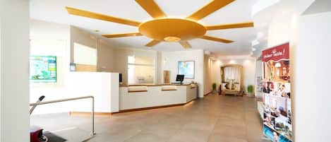 A hotel reception area with a modern design, including a reception desk, a large ceiling fan, and a poster on the wall.