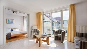 A modern hotel room with a bed, a wooden coffee table, striped armchairs, and a balcony with yellow curtains. - Appartementhaus Haus Strandperle (Zinnowitz)