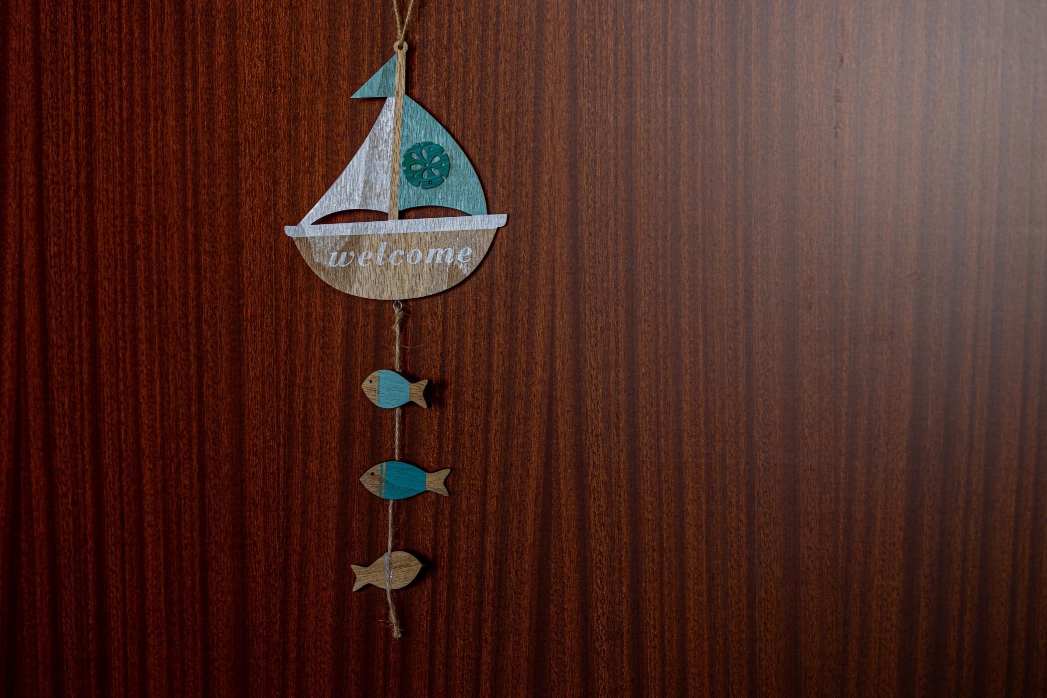 Ein hölzernes Wandbild mit einem Segelboot und dem Schriftzug 'welcome' vor rustikalem Holz.