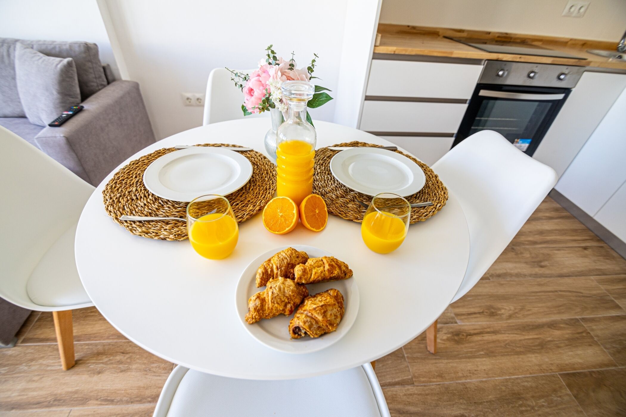 A breakfast setup with croissants, orange juice, and a vase of flowers on a white table in a modern kitchen.