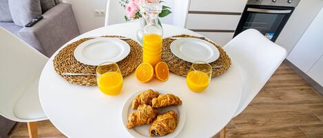 A breakfast setup with croissants, orange juice, and a vase of flowers on a white table in a modern kitchen.