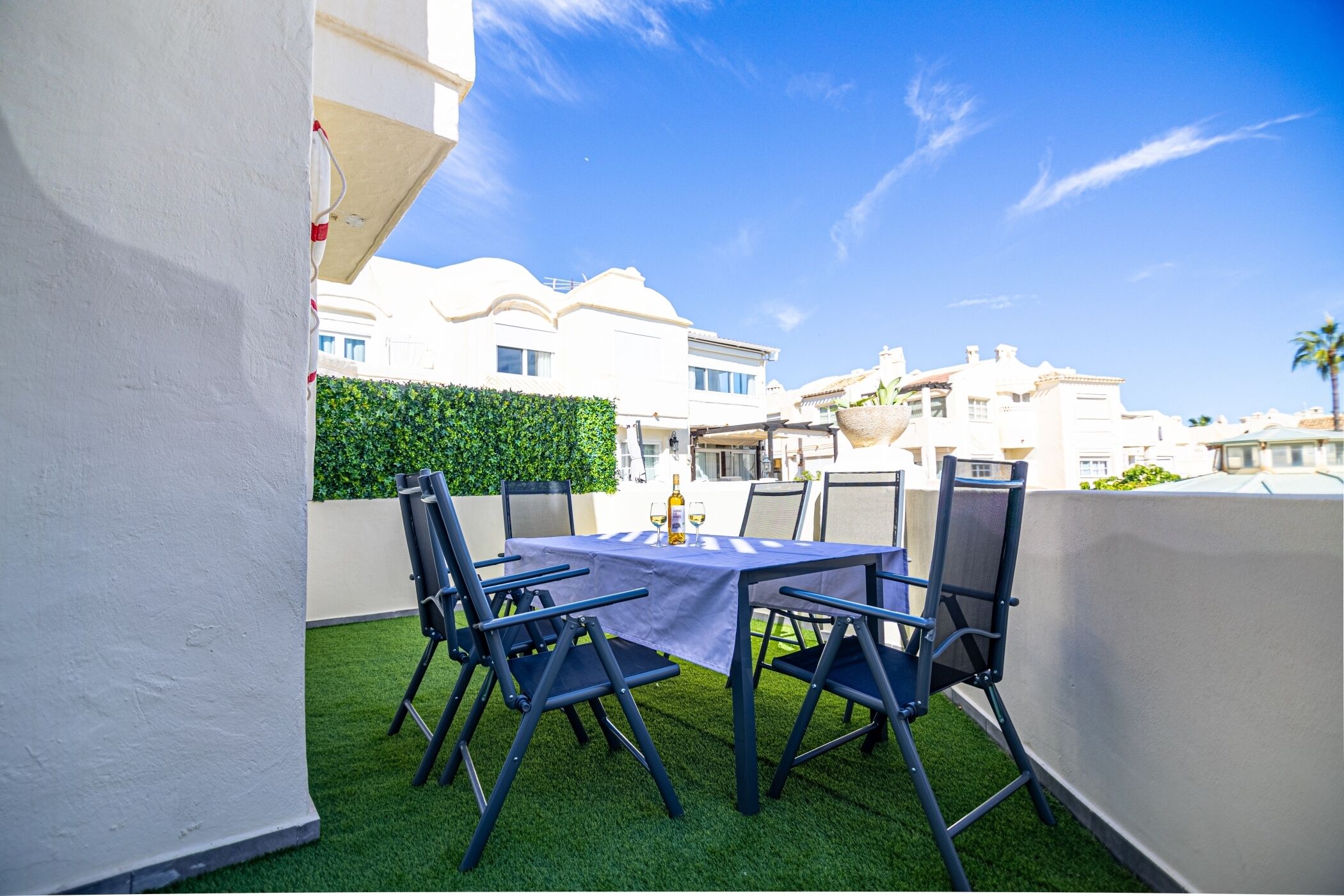 A rooftop terrace with a table and chairs, a bottle of wine, and a view of surrounding buildings.