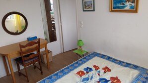 A room with a wooden desk, a chair, a bed with a floral quilt, a mirror, a green lamp, and two framed pictures on the wall. - Apartement de 1 à 4personnes 200m de la mer (La Turballe)