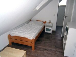 A small, single-bed room with a wooden bed, a bedside table, a nightstand, and a wardrobe. - Pommernweg 15 Merchant (Wangerland)