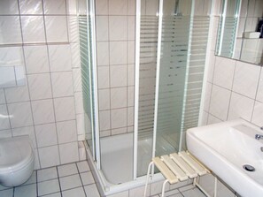 A bathroom with a toilet, a glass shower enclosure, and a sink with a handheld showerhead. - Pommernweg 15 Merchant (Wangerland)