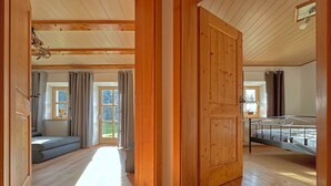 A spacious room with a wooden floor, a bed, a window with curtains, and a door leading to another room. - Ferienwohnung im Bayerischen Wald mit Terrasse (Viechtach)