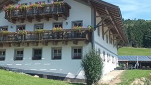 A multi-story building with balconies adorned with flowers, a sloped roof, and a solar panel array in the background. - Ferienwohnung im Bayerischen Wald mit Terrasse (Viechtach)