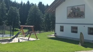 A building with a large mural, a swing set, and a fenced play area. - Ferienwohnung im Bayerischen Wald mit Terrasse (Viechtach)