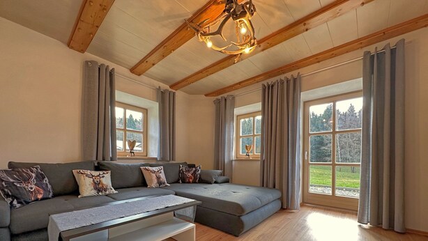 A modern living room with a sectional sofa, a coffee table, and large windows with curtains. - Ferienwohnung im Bayerischen Wald mit Terrasse (Viechtach)