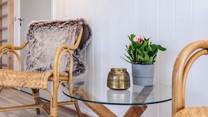 A wicker chair with a fur throw, a glass table with a brass vase and a potted plant, and a wooden door in the background. - 4 Star Holiday Home in Hjorring (Hjørring)
