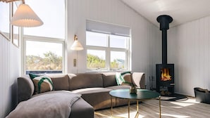 A modern living room with a sectional sofa, a round coffee table, and a wood-burning stove. - 4 Star Holiday Home in Hjorring (Hjørring)