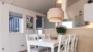 A dining area with a white table and chairs, a vase with flowers, and a window with blinds. - 4 Star Holiday Home in Hjorring (Hjørring)